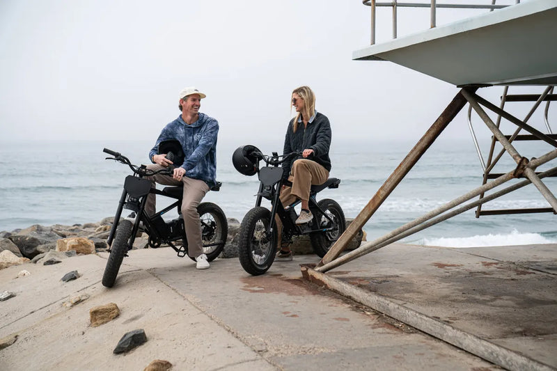 Two riders laughing on STACYC 20hDRIVE e-bikes next to a lifeguard tower