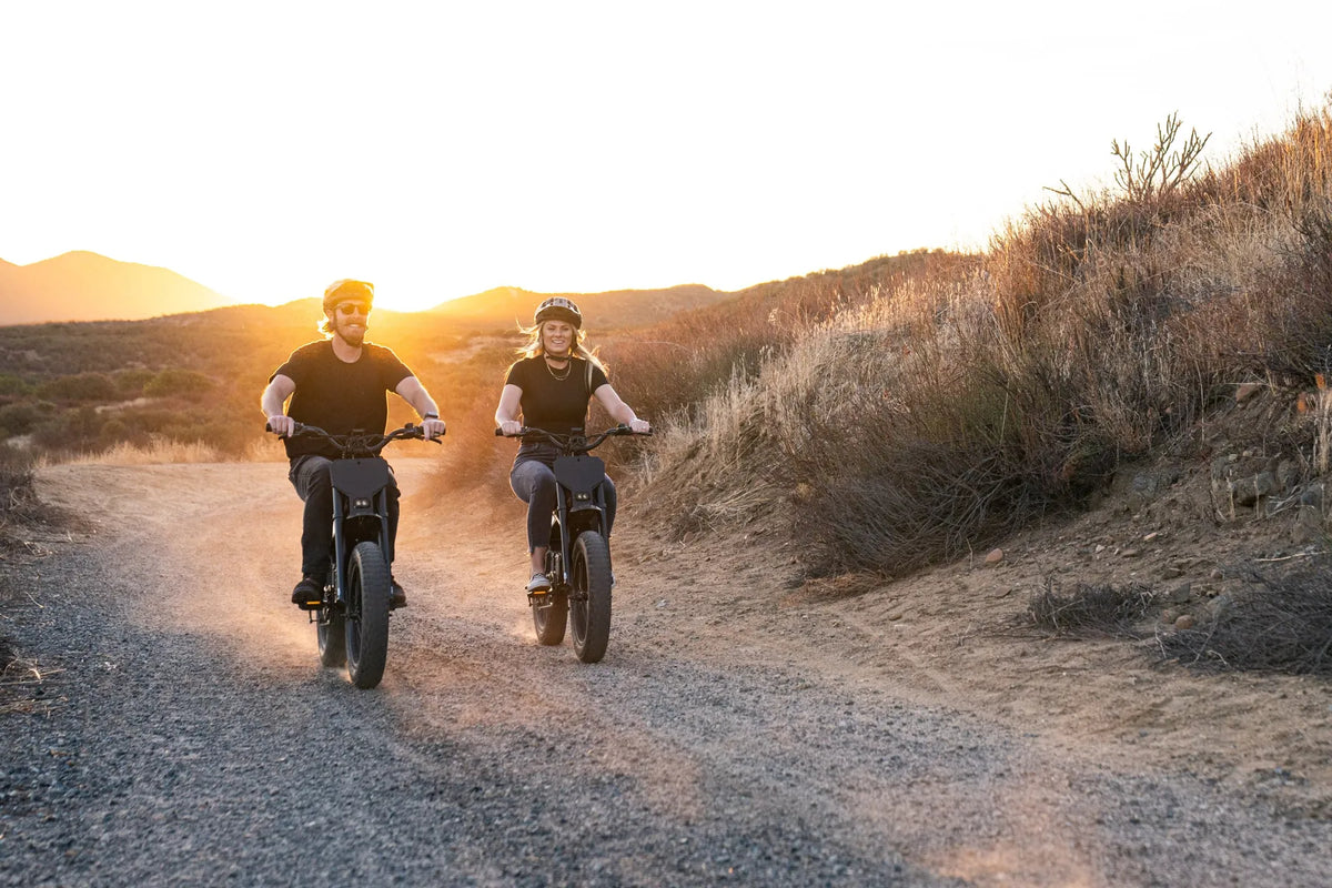 Two riders on STACYC 20hDRIVE e-bikes kicking up dust on a dirt trail at sunset